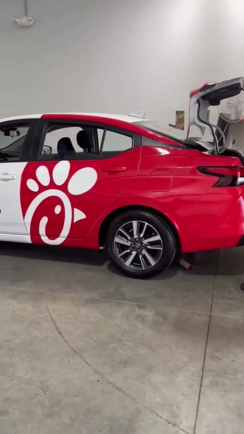 A red and white liveried fleet car being worked on inside the shop bay, trunk open, concrete floor