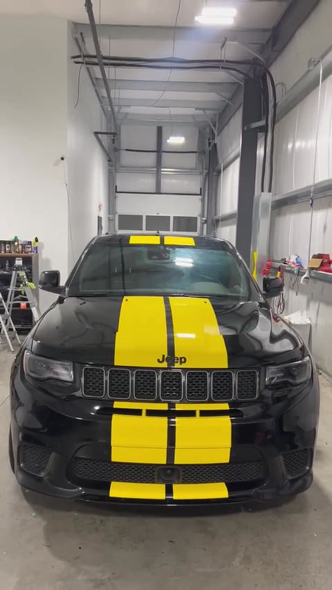 The inside of the Mo Tint workshop: sealed concrete floor, overhead lighting, closed roller door, supply shelving, with a black Jeep Trackhawk parked in the middle