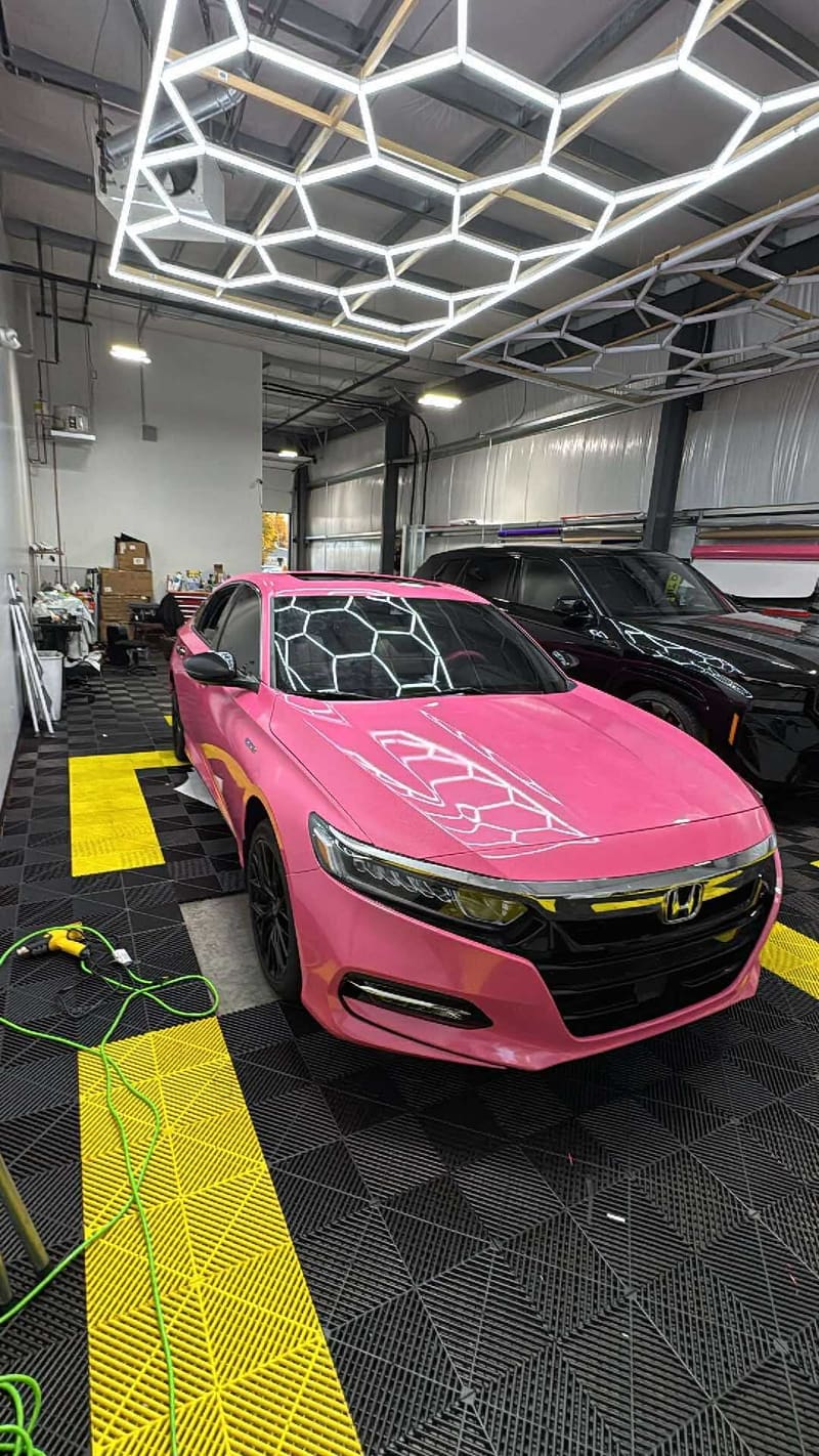 Honda Accord in a hot pink gloss wrap with white honeycomb hood graphics, parked under the hexagon LED grid inside the Mo Tint bay