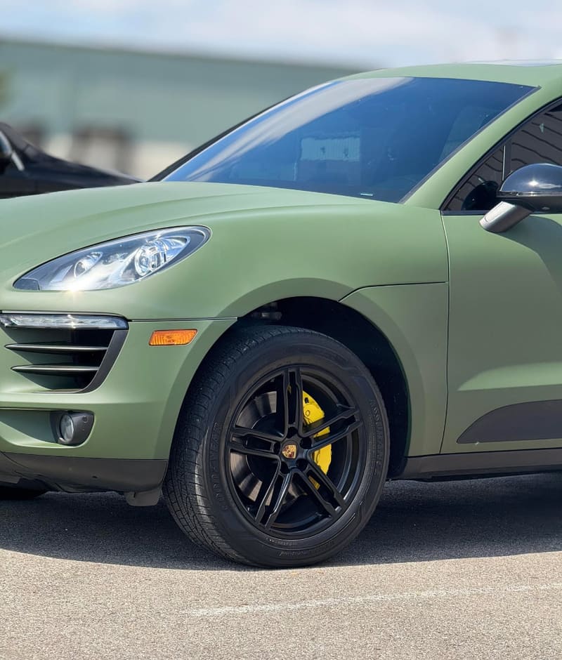 Front wheel of a matte green Porsche Macan with a gloss black rim and yellow-painted caliper