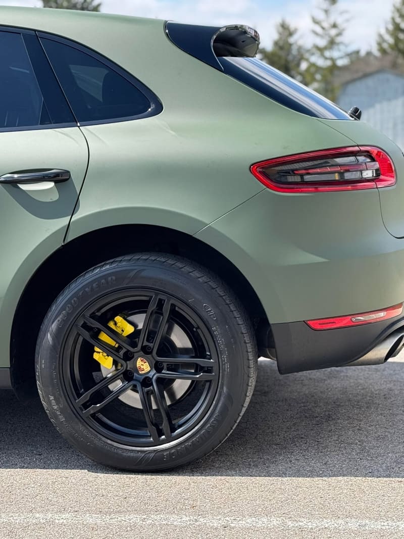 Rear quarter of a matte green Porsche Macan showing a gloss black wheel with a yellow caliper behind the spokes
