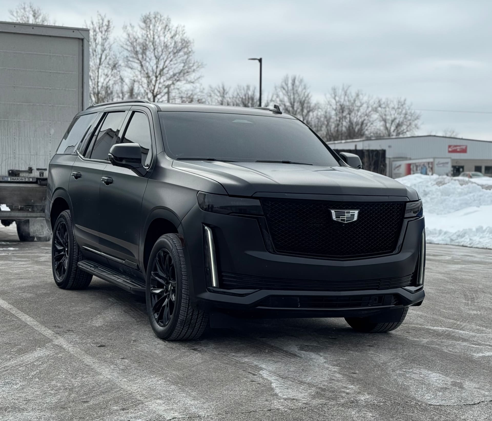 Satin black Cadillac Escalade with blacked-out grille, window trim, badges and wheels, parked on a snowy Ohio commercial lot