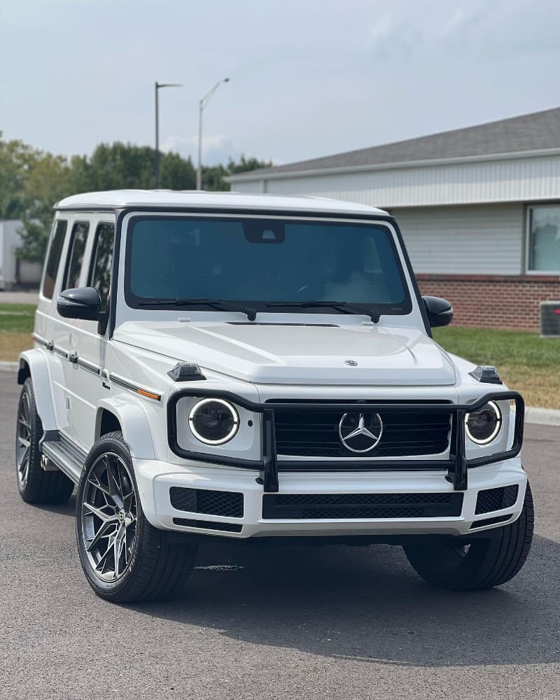 White Mercedes-Benz G550 with blacked-out grille surround, brush guard, mirror caps and side trim, on grey aftermarket wheels