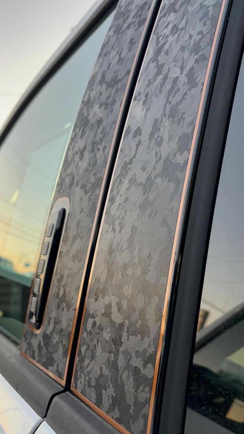Close-up of a car's B-pillar finished in dark forged-carbon vinyl, with the cut line visible around the door handle