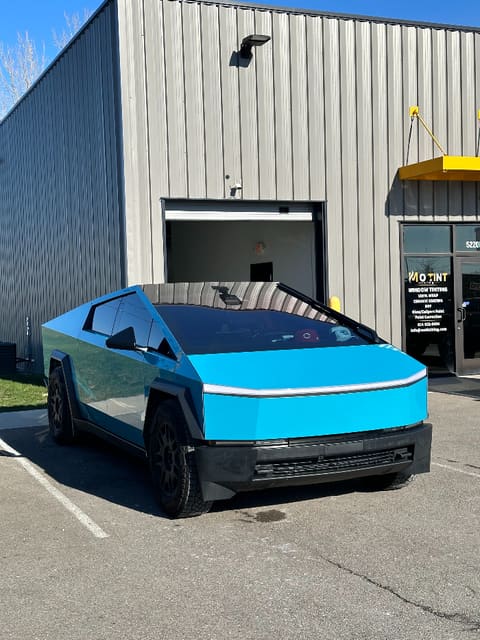 Tesla Cybertruck in a bright blue wrap parked outside the shop, the MO TINT KING window sign and unit number 5220 visible behind it