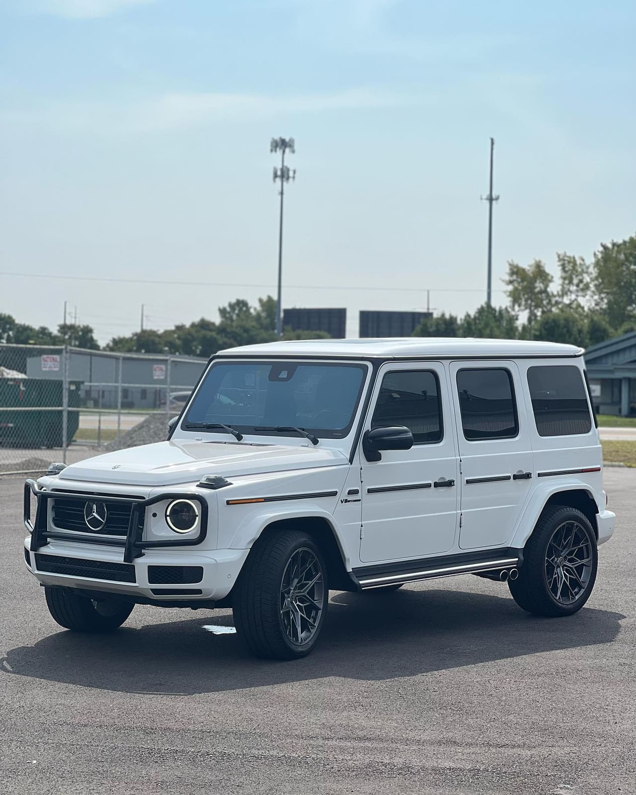White Mercedes-Benz G-Class on gloss black multi-spoke wheels, three-quarter front, parked on an open lot