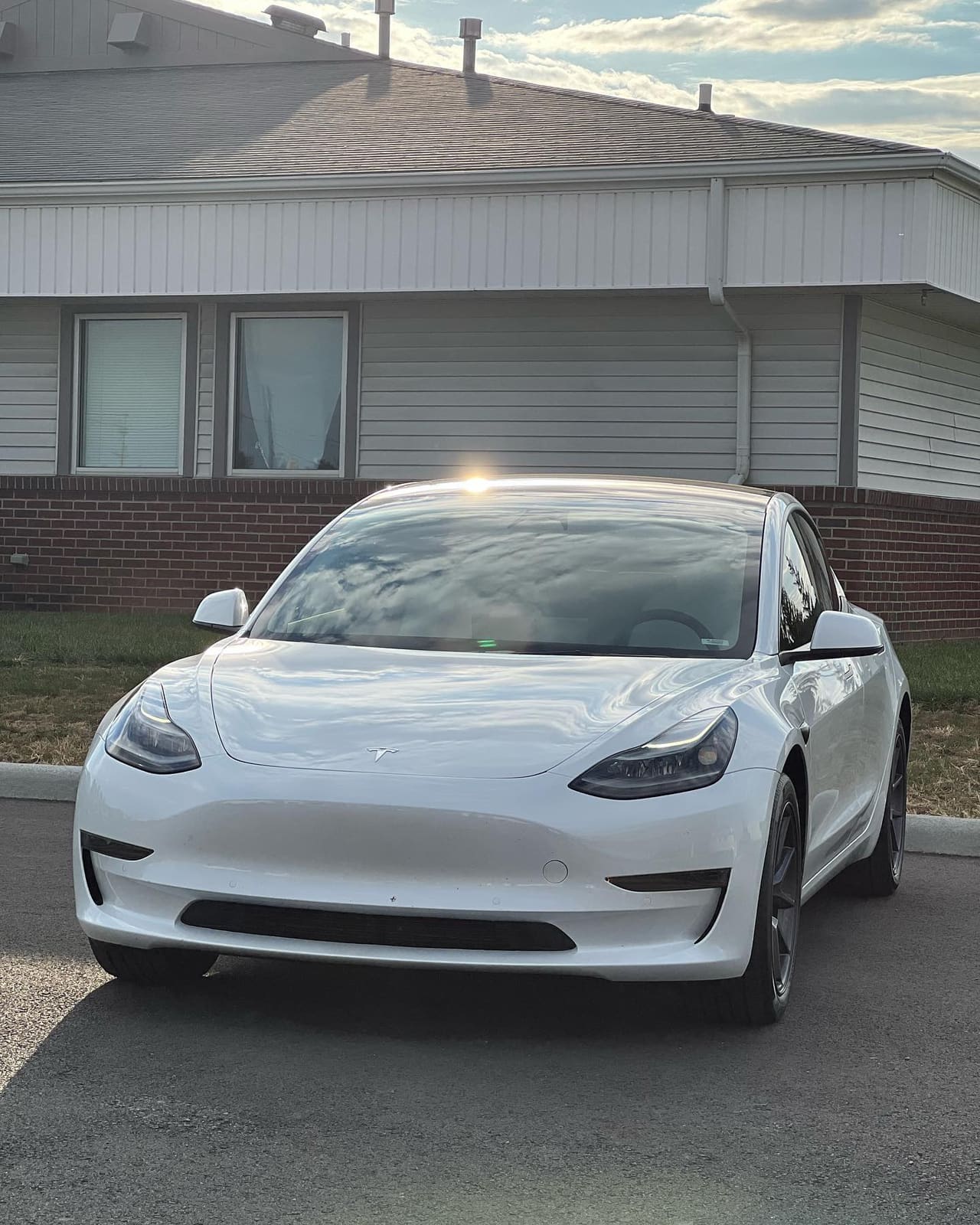 White Tesla Model 3 with tinted glass, front three-quarter at golden hour