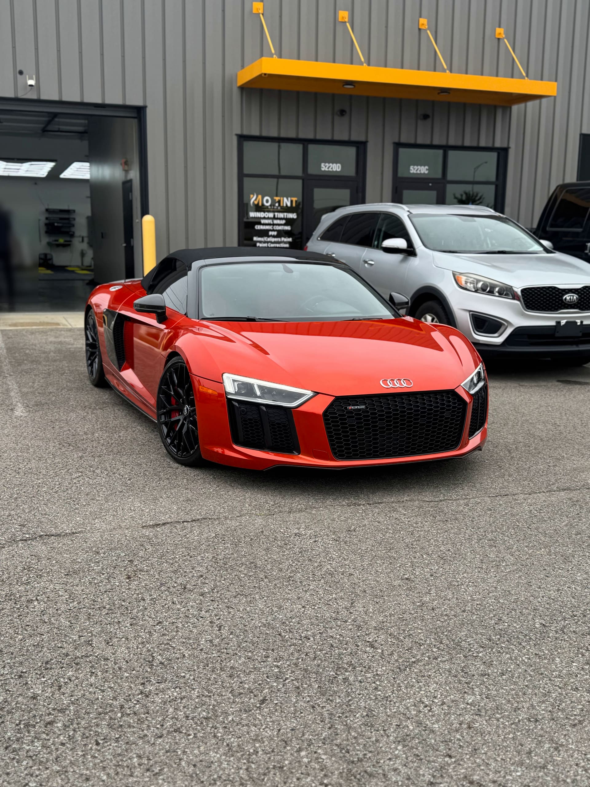 Red Audi R8 Spyder parked at Mo Tint's open bay door, the MO TINT sign behind it listing window tinting, vinyl wrap, ceramic coating, PPF, rims and calipers paint and paint correction, units 5220D and 5220C legible on the glass