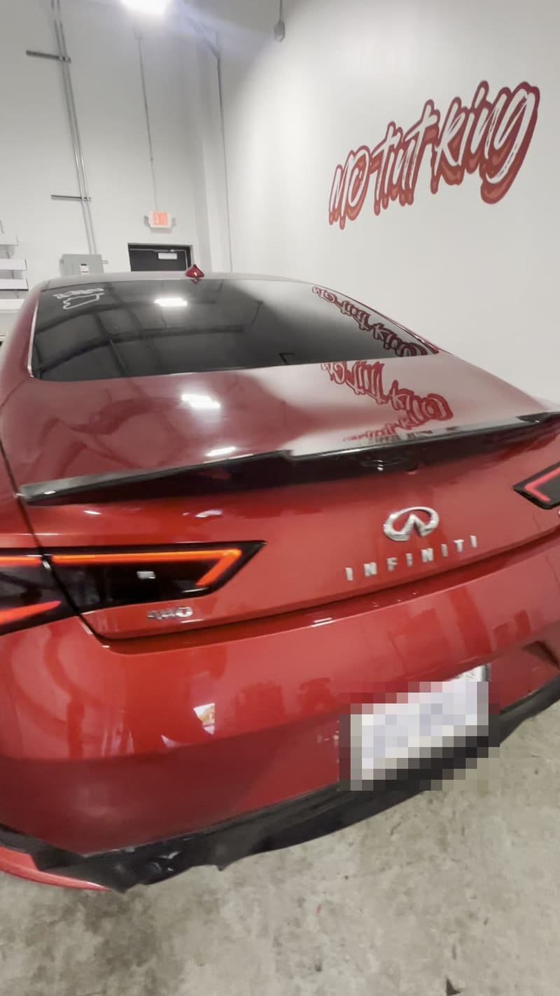 Inside the Mo Tint bay: a deep red Infiniti with fresh window tint and Mo Tint King decals across the rear glass, the hand-painted MO TINT KING mural on the wall behind, sealed concrete floor and a lit EXIT sign