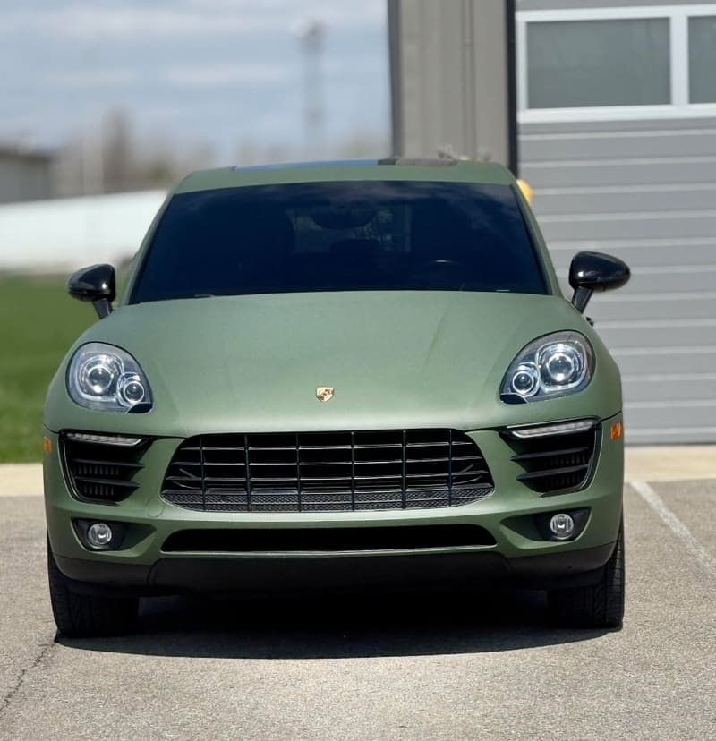 Porsche Macan in a matte military green wrap, dead-on front view beside a roller door