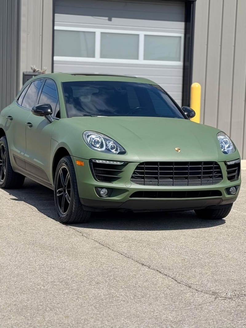 Matte army green Porsche Macan parked directly in front of the shop's white roller door