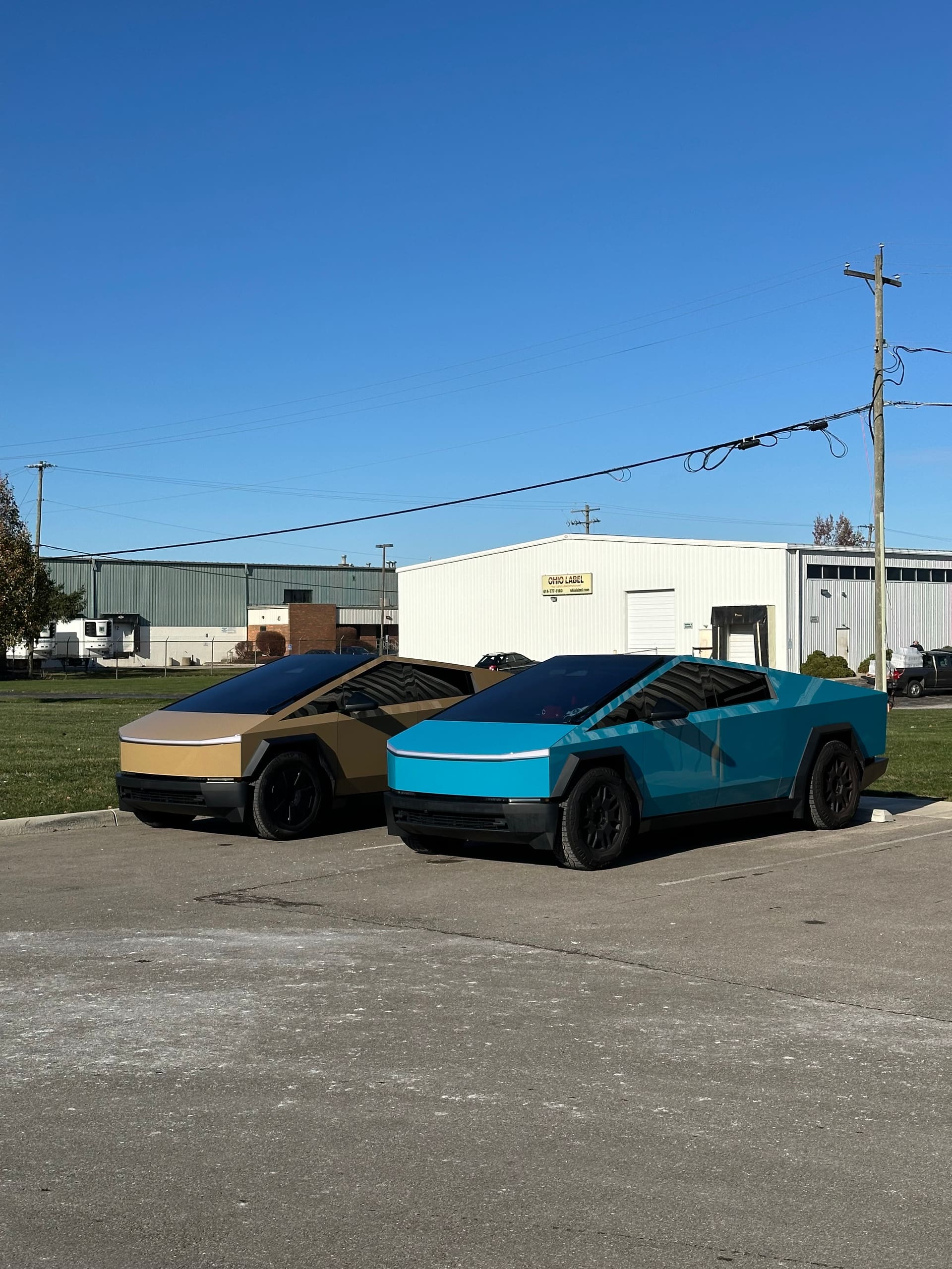 Two wrapped Tesla Cybertrucks side by side in the lot, one bronze and one cyan