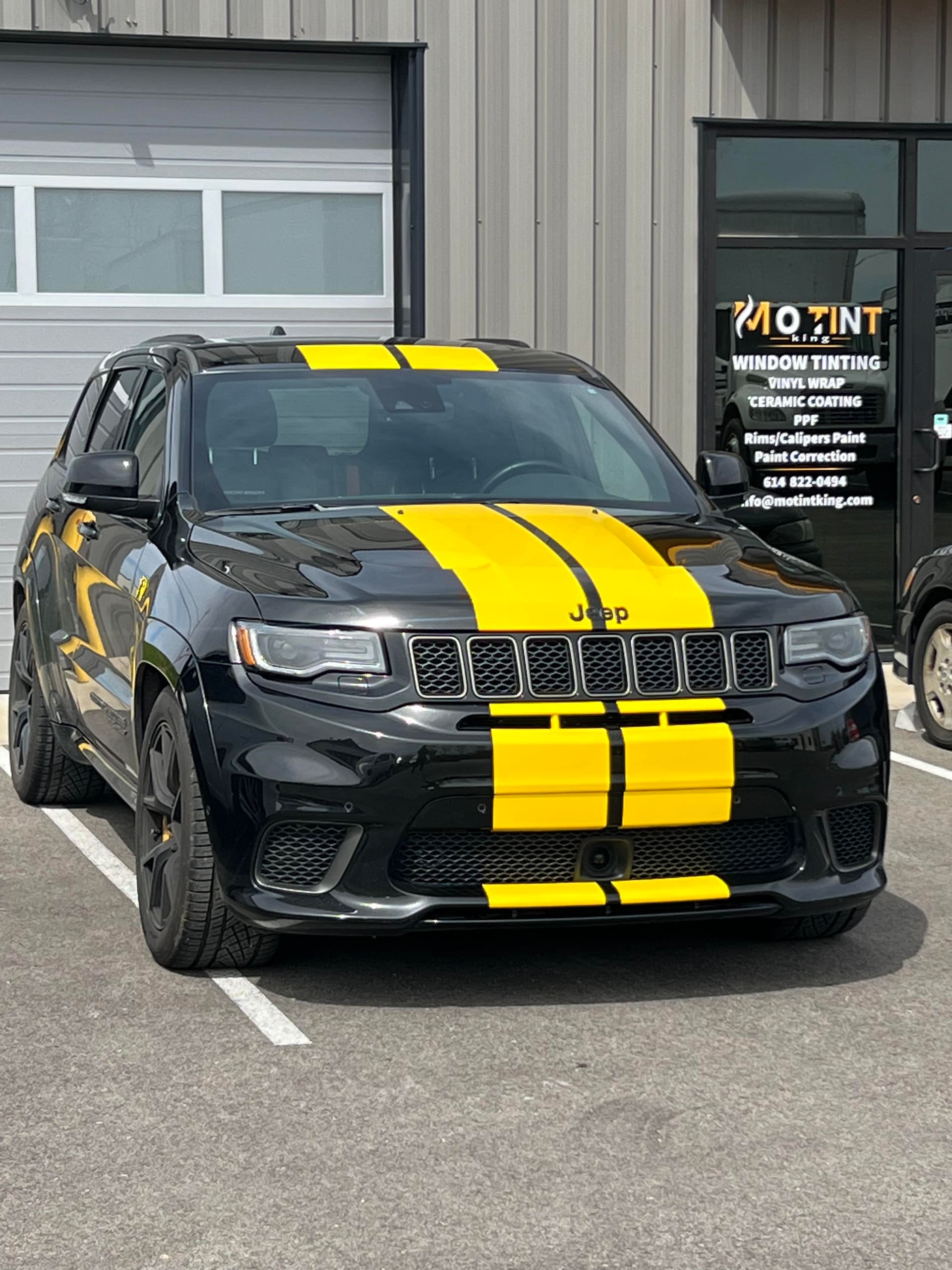 Black Jeep Trackhawk with yellow racing stripes parked at the shop entrance, the MO TINT KING door decal listing every service beside it