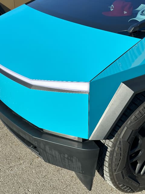 Close-up of the cyan-wrapped Cybertruck's front corner showing the vinyl finish and the edge work along the light bar