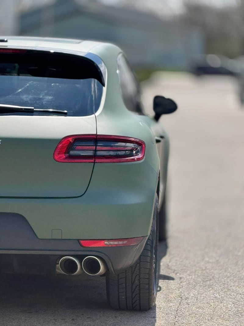 Rear three-quarter detail of a Porsche Macan in matte military green wrap, showing the tailgate, quad exhausts and rear wheel